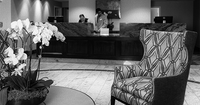 Black and white image of the lobby chair and table with the front desk in the background.